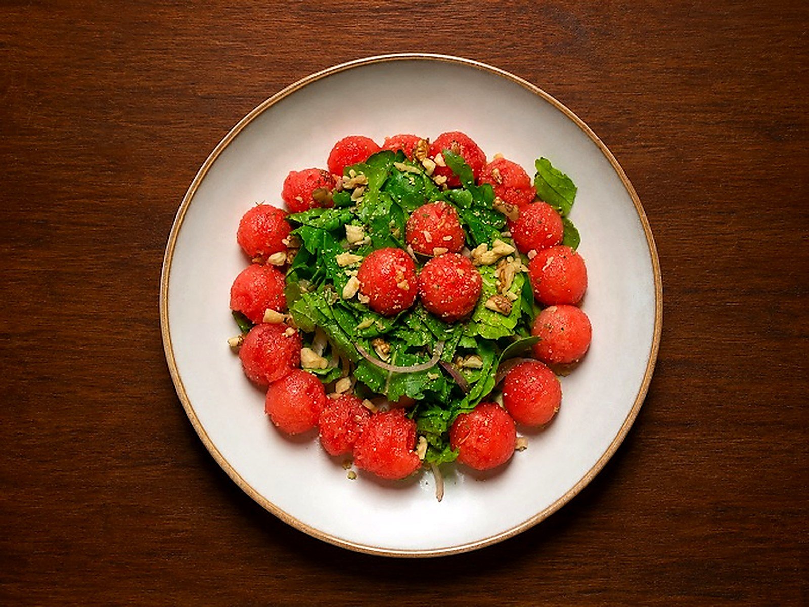 Watermelon and greens salad plated on a dark wooden table